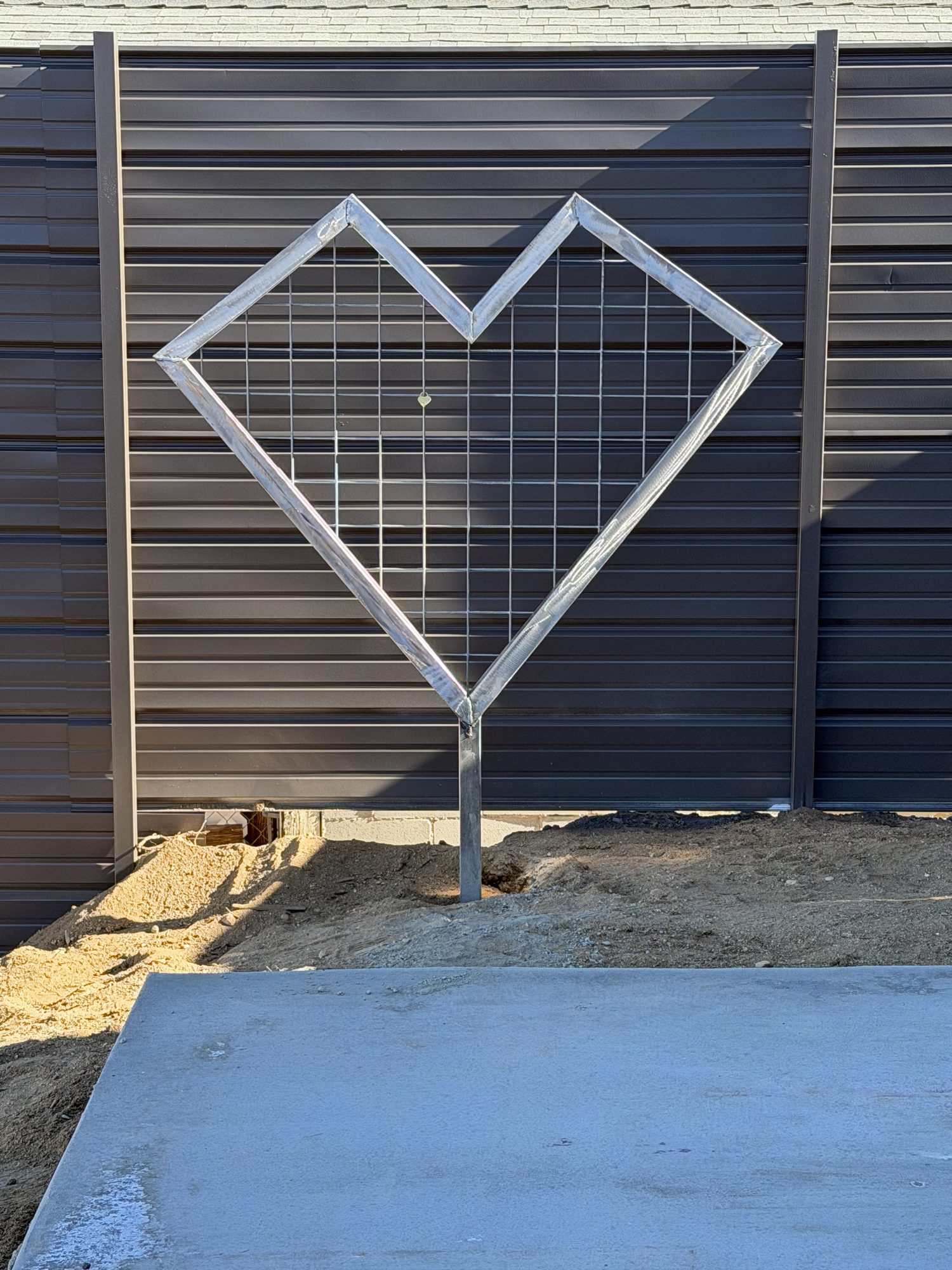 Custom heart-shaped steel trellis mounted on dark metal siding