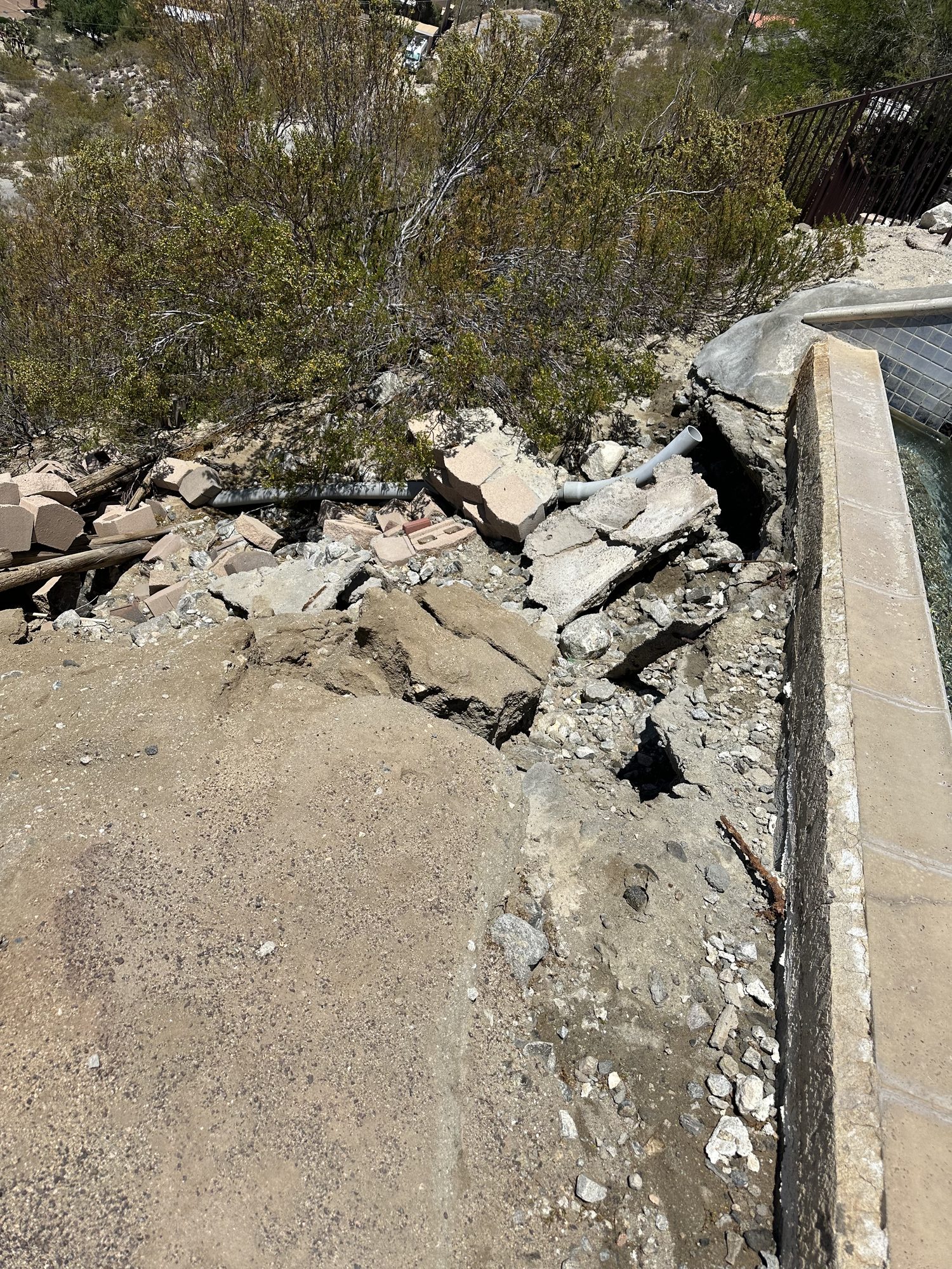 Broken concrete and undermined ground beside a retaining wall